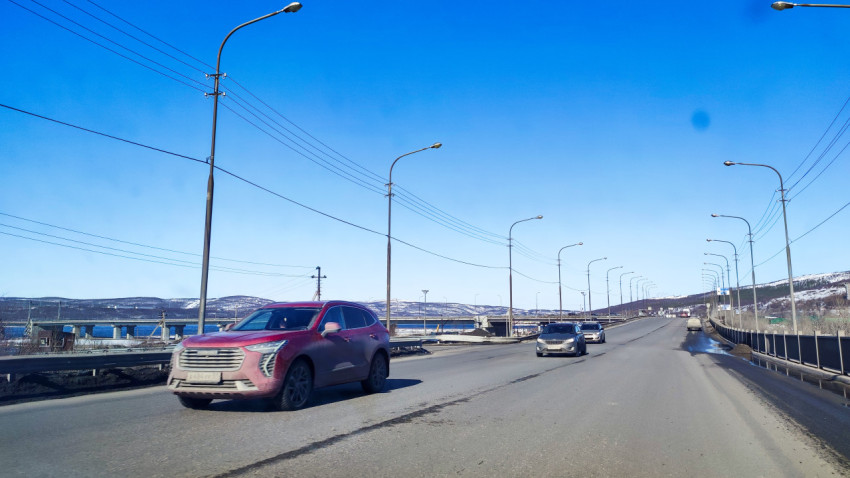Автомобили на мосту через водоем на фоне заснеженных холмов