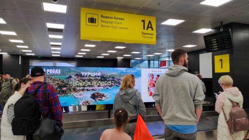 Зона выдачи багажа с указателем и рекламными экранами в аэропорту Казани