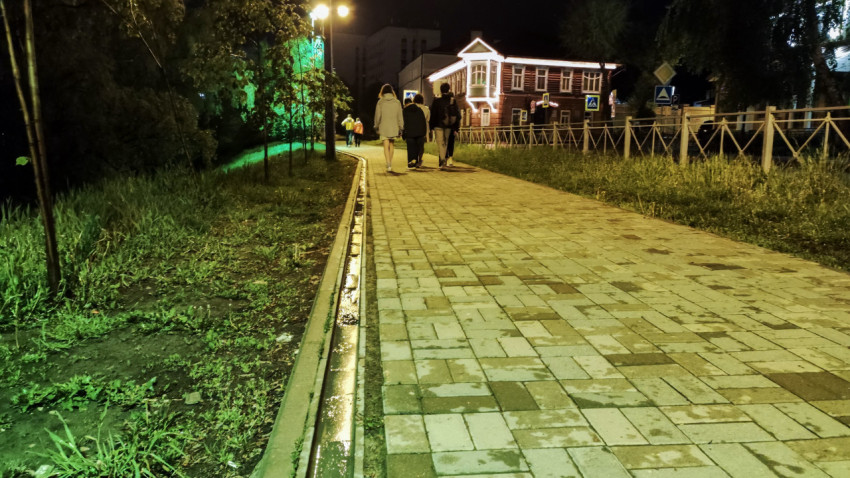 Пешеходная дорожка с фонарями и группой людей на фоне дома с подсветкой