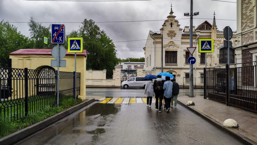 Пешеходы с зонтами на фоне дорожных знаков и перехода