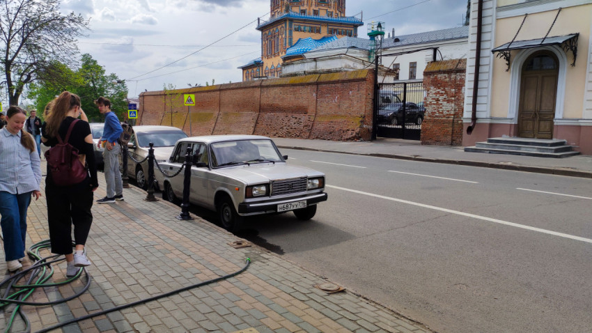 Пешеходы и припаркованные автомобили у исторического здания