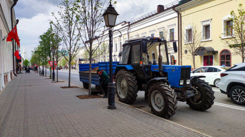 Рабочий разгружает трактор с прицепом на городской улице