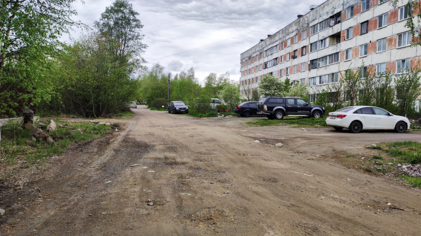 Грунтовая дорога возле жилого дома и припаркованных автомобилей