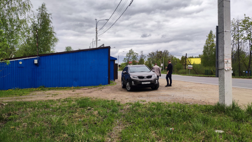 Автомобиль у синего ангара и двое мужчин на обочине