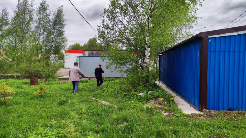 Двое мужчин идут по зелёной территории возле синего ангара