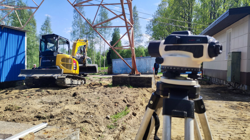 Экскаватор Komatsu и геодезический прибор возле опоры ЛЭП