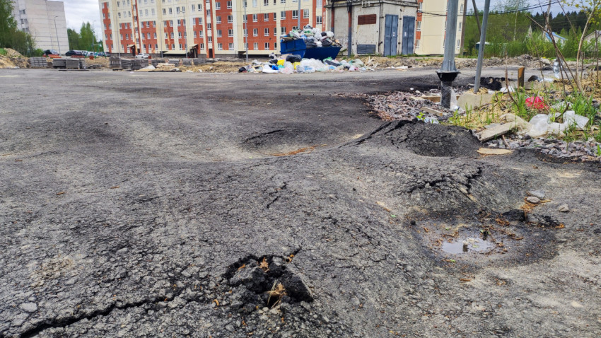 Повреждённый асфальт и переполненный мусорный контейнер во дворе
