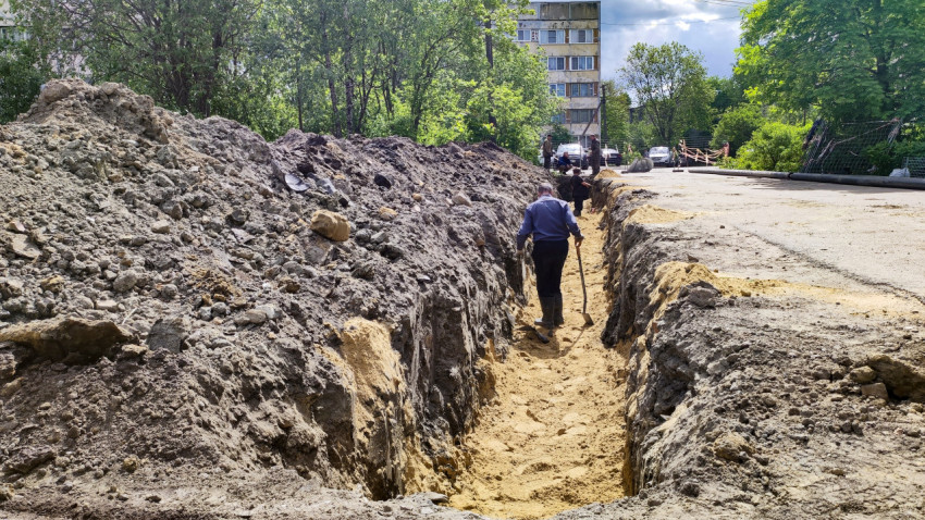 Рабочие в траншее при прокладке трубопровода во дворе жилого дома
