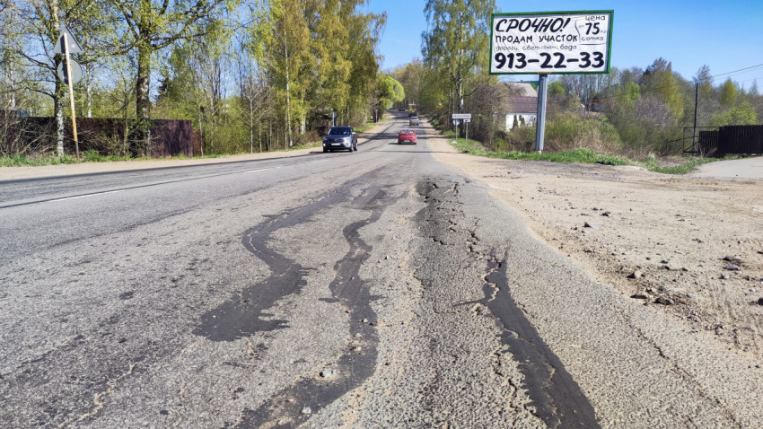 Повреждённый асфальт и реклама на щите вдоль загородной трассы