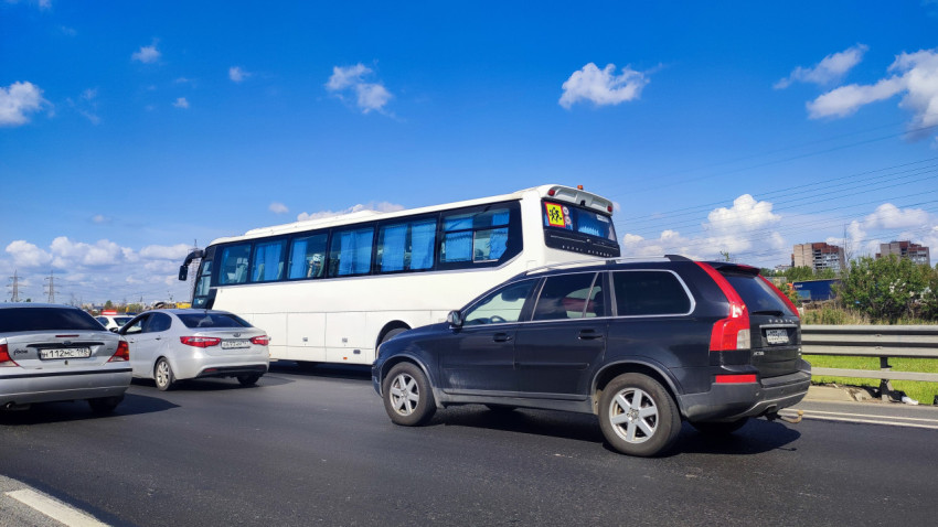 Белый туристический автобус и легковые авто в потоке на шоссе