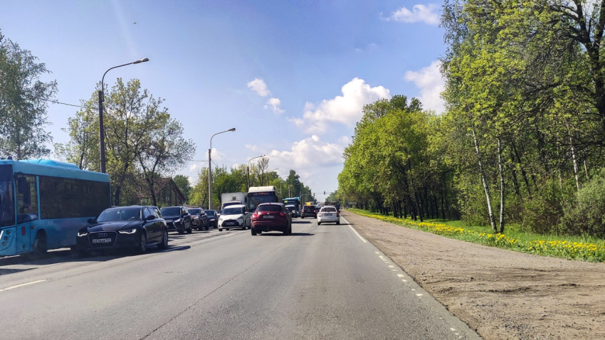 Широкая улица с автобусом и плотным потоком, грунтовой обочиной и зелёной полосой