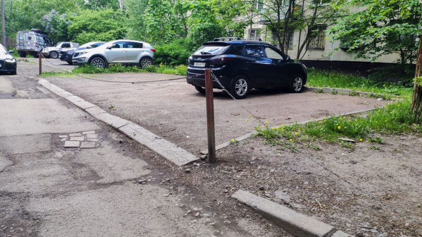 Полупустая дворовая парковка, ограждённая цепью