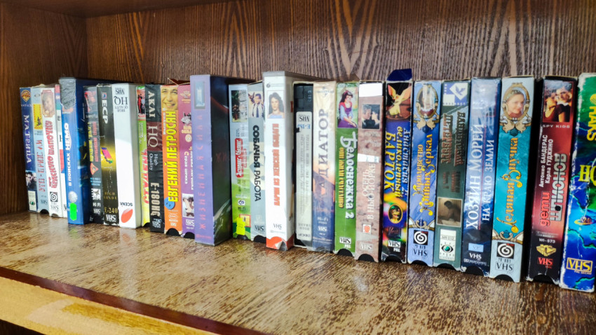 Коллекция VHS-кассет с зарубежными и российскими фильмами на деревянной полке