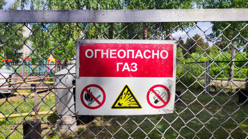 Табличка «Огнеопасно газ» крупным планом на сетчатом заборе