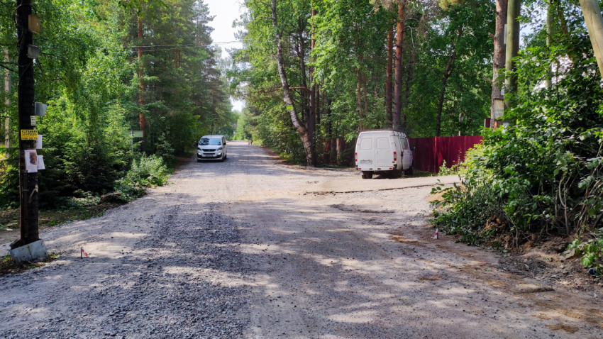 Дорога с гравийным покрытием и припаркованными машинами в посёлке