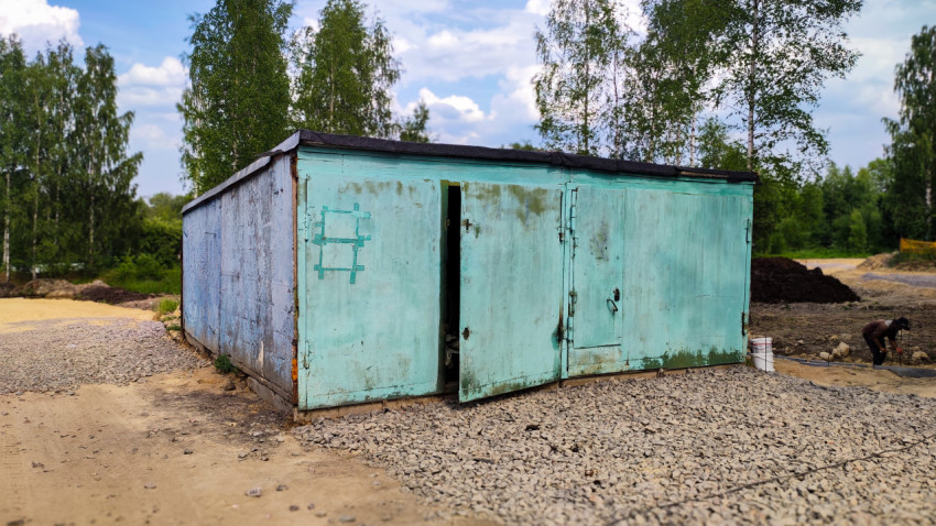Металлический гараж с открытой дверью на щебёночной площадке
