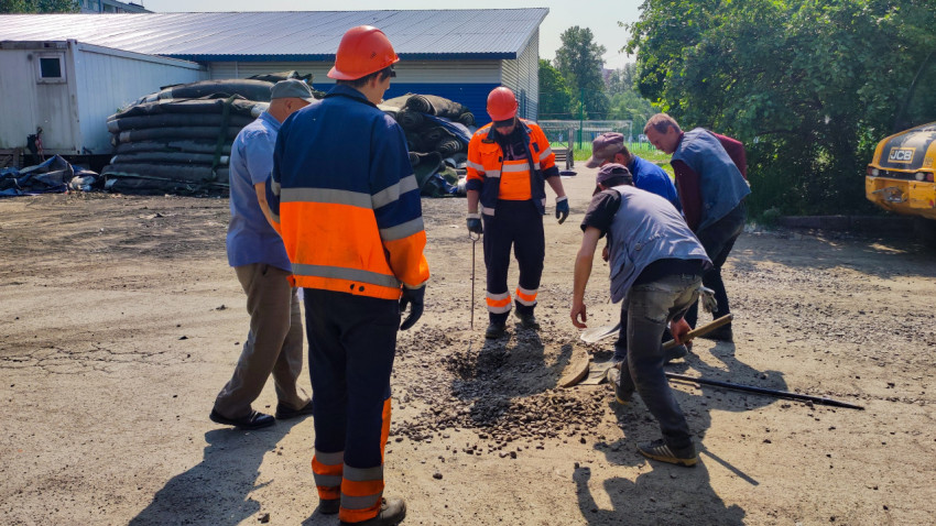Рабочие открывают крышку колодца во дворе жилого квартала