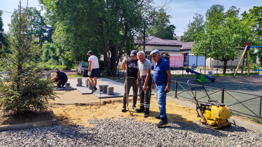 Рабочие укладывают тротуарную плитку возле детской площадки