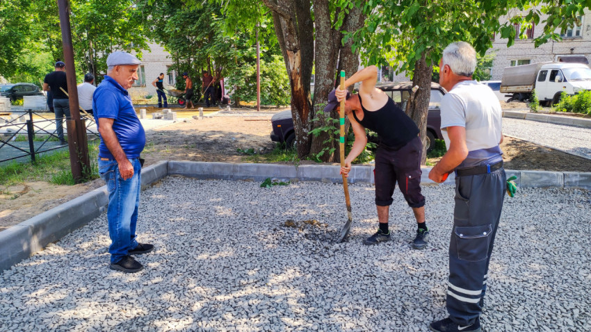 Рабочие готовят основание под тротуар возле деревьев