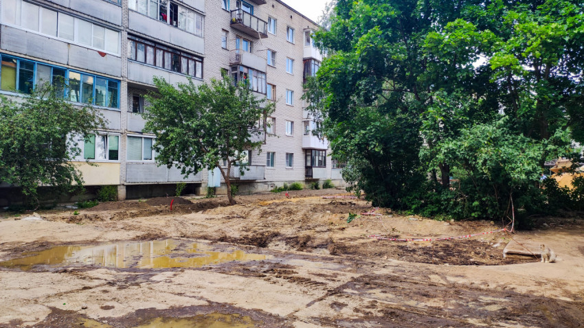 Двор жилого дома после дождя с лужами и земляными работами