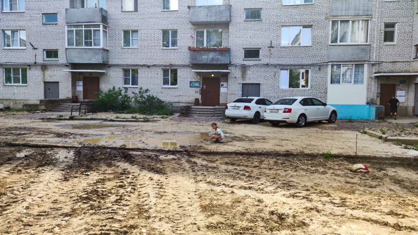Двор жилого дома с ребенком у лужи после земляных работ