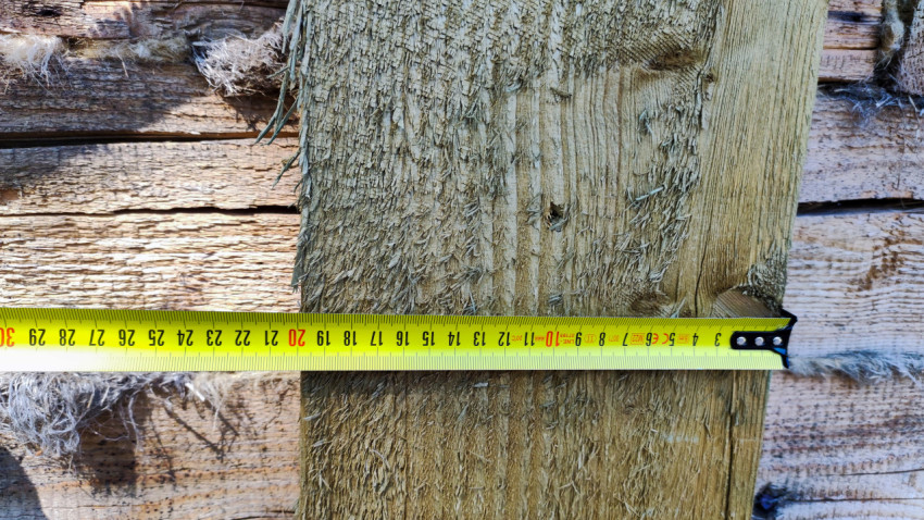 Замер толщины деревянного бруса на стене дома