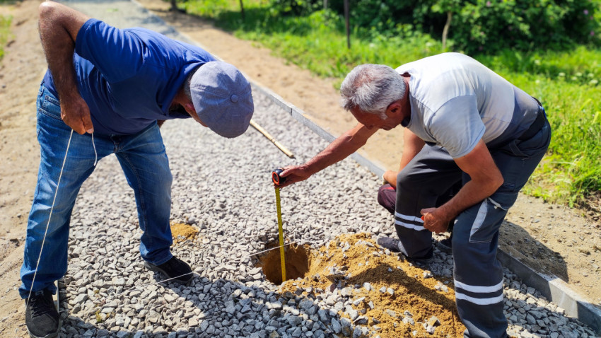 Два рабочих измеряют глубину выкопанной ямы на тротуаре