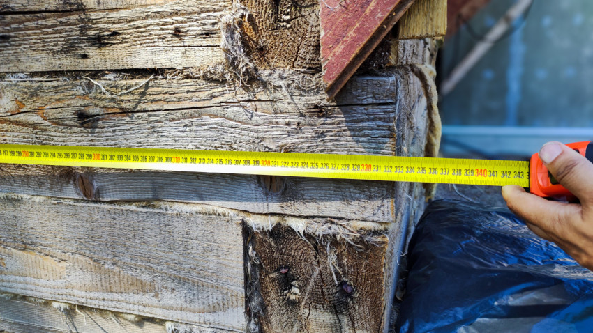 Замер длины деревянной стены дома с помощью рулетки