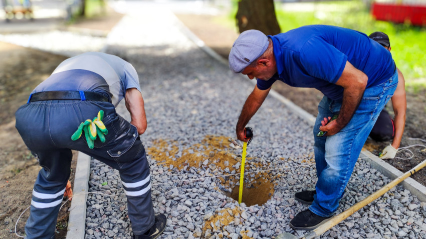 Рабочие измеряют глубину ямы на щебёночной дорожке