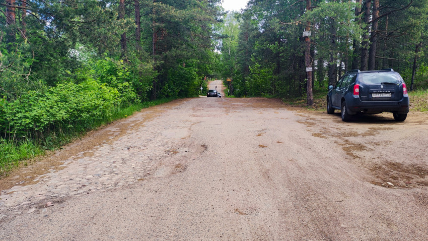 Дорога с поврежденным покрытием и автомобилями на обочине в лесной зоне