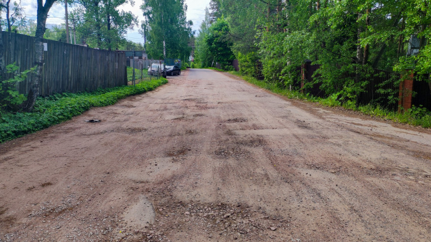 Грунтовая дорога с выбоинами вдоль деревянного забора