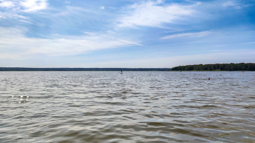 Человек на сапборде и отдыхающие в воде на озере