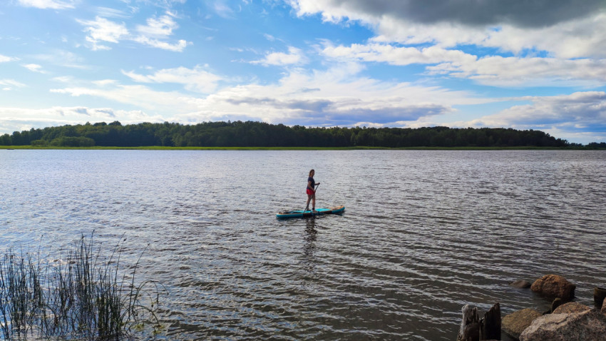 Женщина на сапборде рядом с берегом и скалами