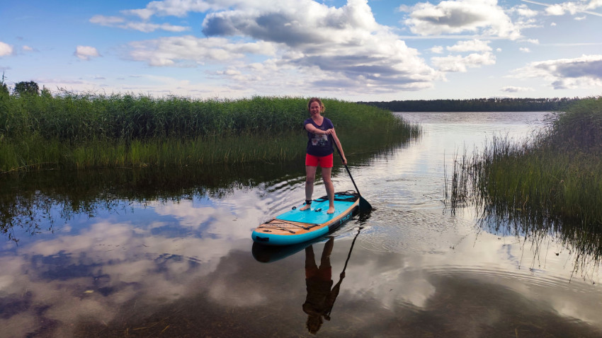 Женщина на сапборде у тростника с отражением в воде