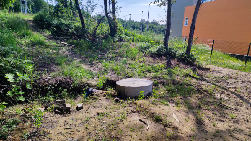 Колодец инженерных сетей на грунтовом участке рядом с застройкой