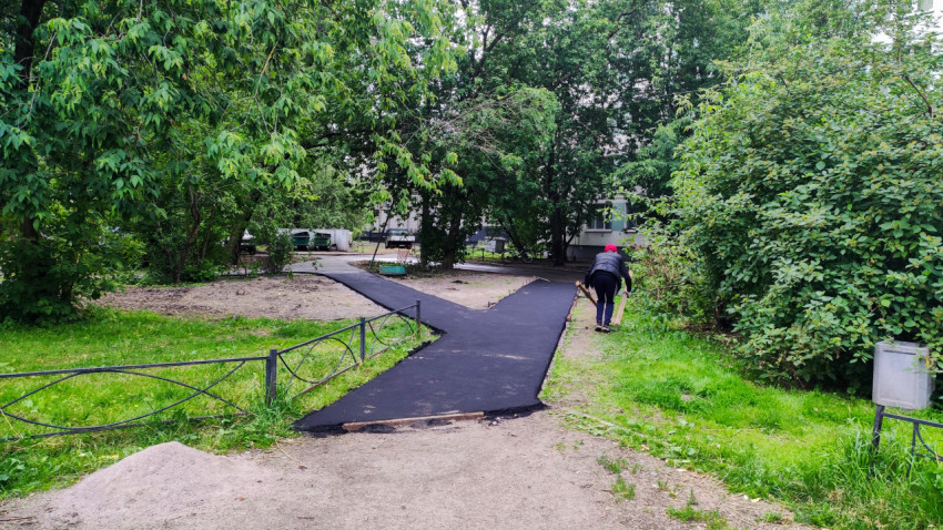 Рабочий укладывает асфальт на пешеходной дорожке во дворе жилого дома