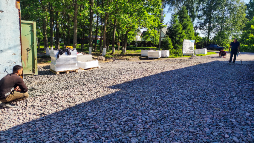 Рабочие и материалы на площадке с щебёночным покрытием