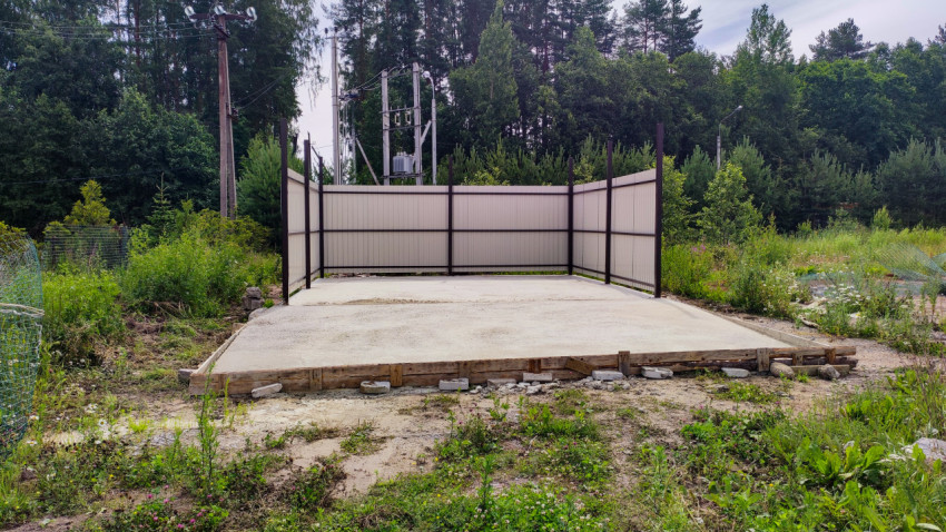 Бетонная площадка в ограждении на фоне леса