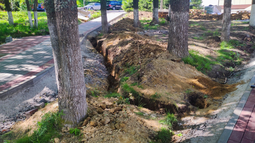Траншея вдоль пешеходной дорожки и деревьев