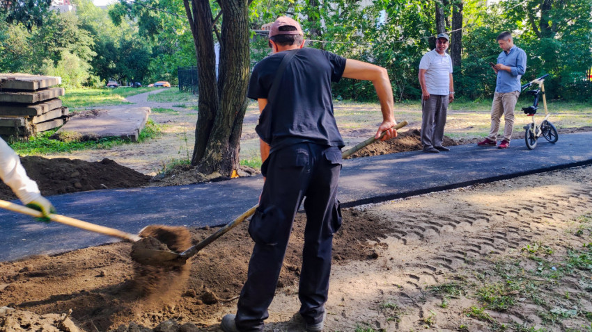 Рабочий засыпает грунт вдоль нового асфальта