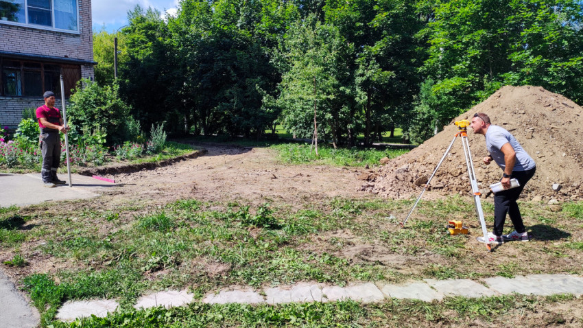 Геодезист с рейкой и инженер с нивелиром во дворе