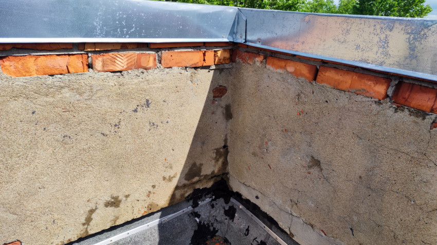 Угол крыши здания с трещинами и следами влаги на стене