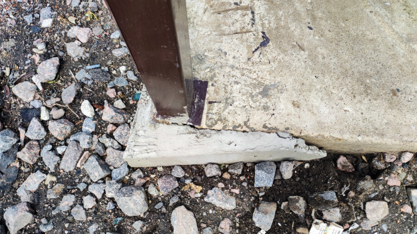 Металлическая опора забора в бетонном основании с трещинами