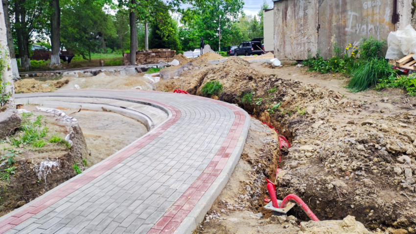 Траншея с кабельными трубами вдоль изгиба тротуара