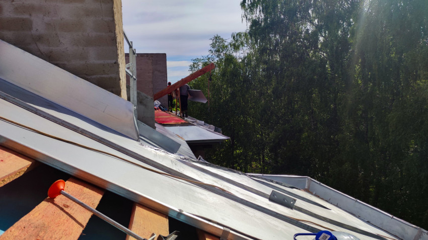 Рабочие поднимают металлические листы на крышу