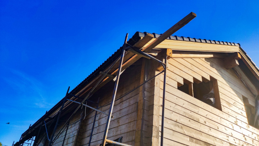 Строительные леса у деревянного дома с крышей из черепицы