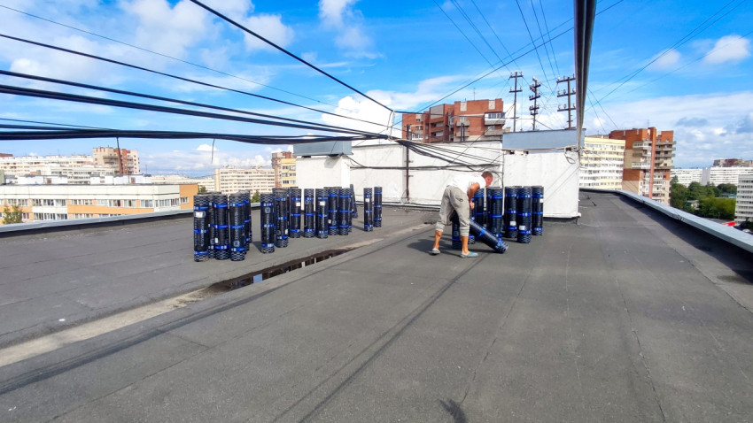 Рабочий на крыше жилого дома с рулонами кровельного материала