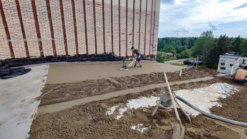Рабочий затирает цементную стяжку на крыше здания