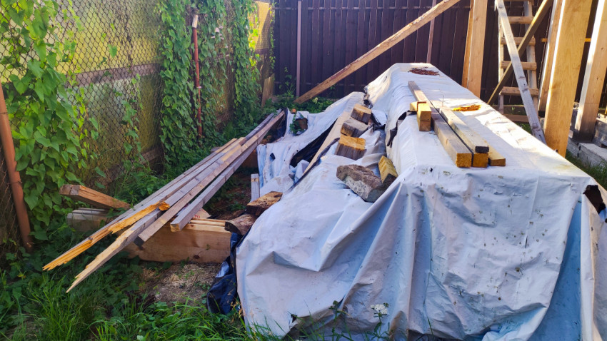 Строительные материалы под защитным тентом возле забора