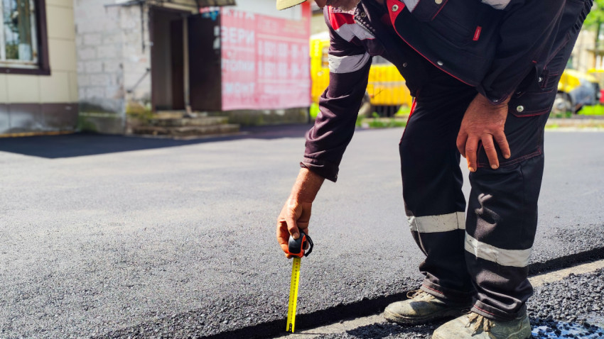 Рабочий измеряет толщину свежего асфальта рулеткой